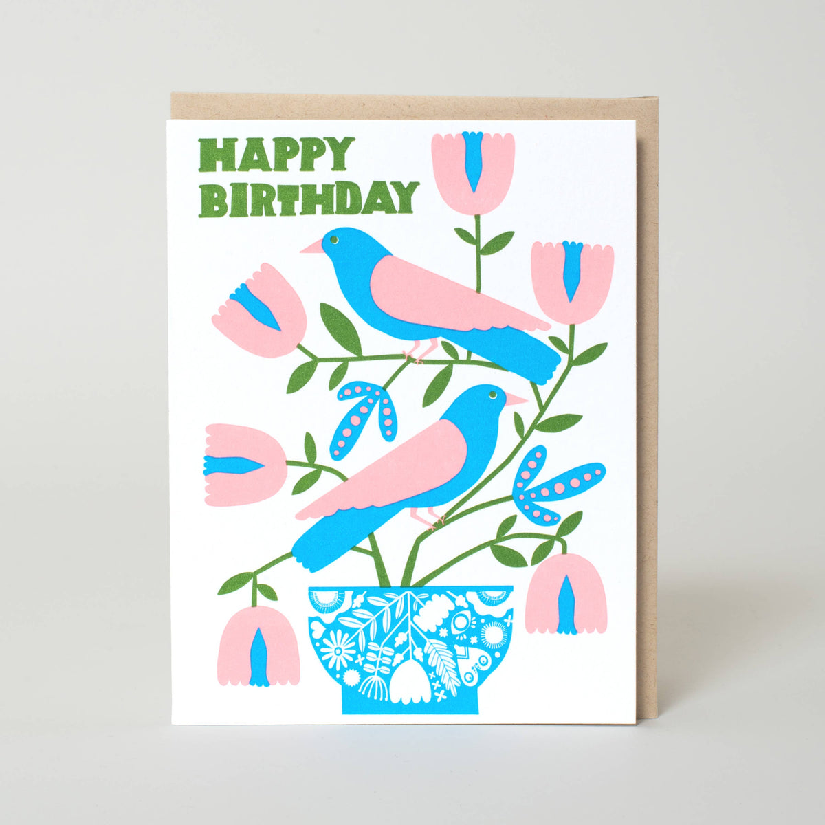 A square birthday greeting card with a kraft envelope, featuring a colorful illustration of two blue and pink birds, pink flowers, green leaves, and a blue patterned vase, with the words 'HAPPY BIRTHDAY' in green at the top. Birds & Florals Birthday Letterpress Greeting Card: by Egg Press